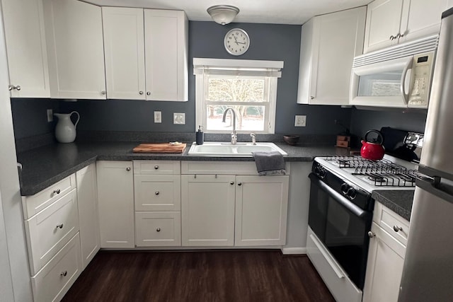 kitchen with dark countertops, white microwave, white cabinetry, a sink, and gas stove