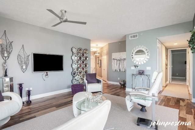 living room featuring dark wood-style floors, visible vents, baseboards, and a ceiling fan