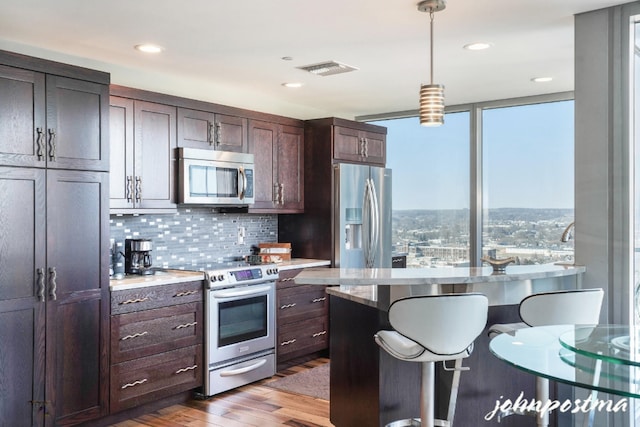 kitchen featuring stainless steel appliances, visible vents, light wood-style floors, tasteful backsplash, and decorative light fixtures