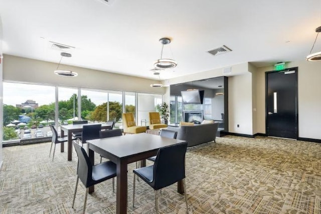 dining room with baseboards, visible vents, light colored carpet, and a glass covered fireplace