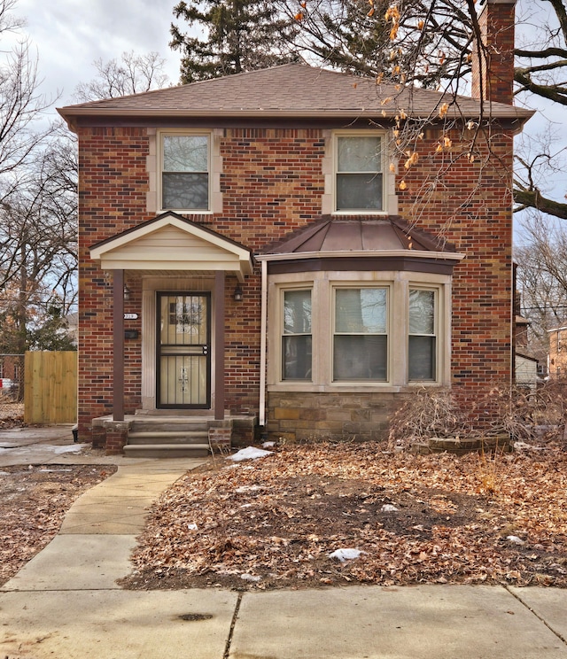 traditional-style house featuring roof with shingles, brick siding, a chimney, and fence