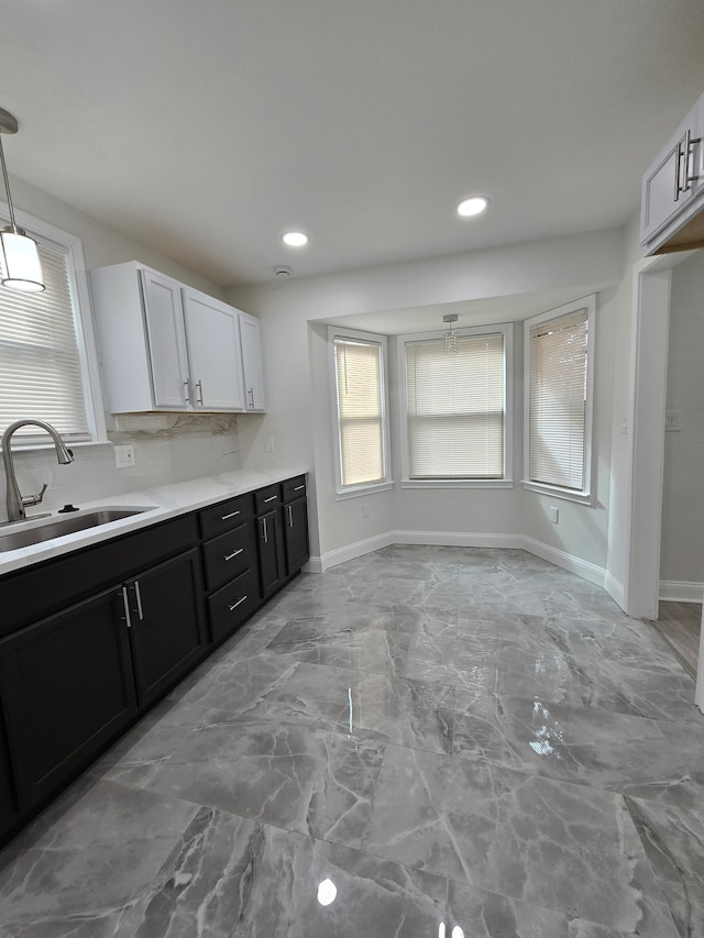 kitchen featuring marble finish floor, tasteful backsplash, light countertops, a sink, and baseboards