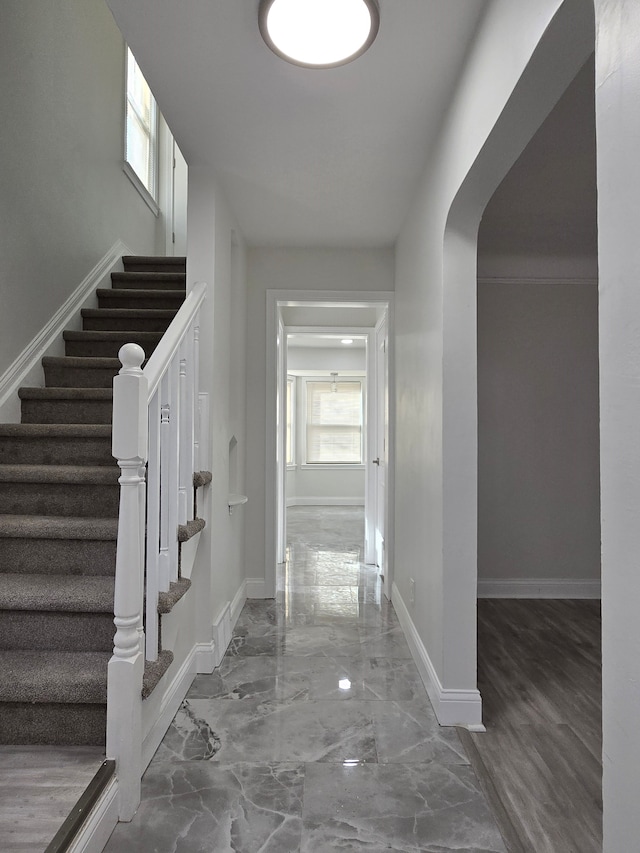 hall featuring arched walkways, marble finish floor, and baseboards