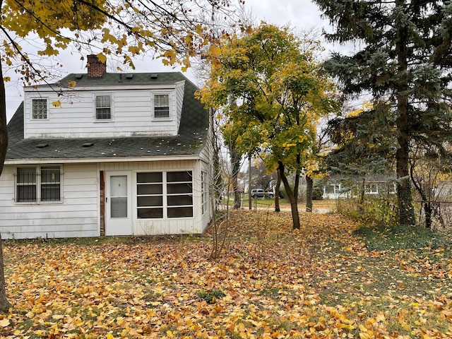 rear view of house featuring a shingled roof and a chimney