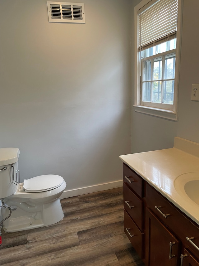 half bath featuring toilet, wood finished floors, vanity, visible vents, and baseboards