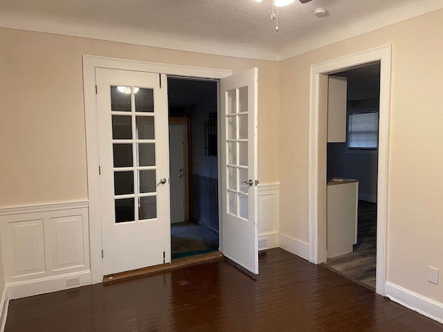 spare room with a wainscoted wall, a ceiling fan, visible vents, and dark wood-type flooring