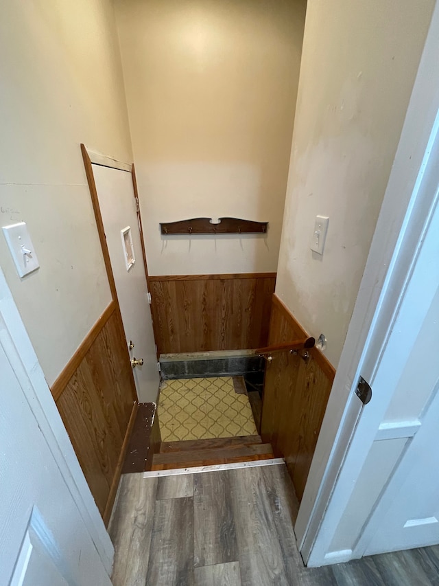 staircase featuring wainscoting, wooden walls, and wood finished floors