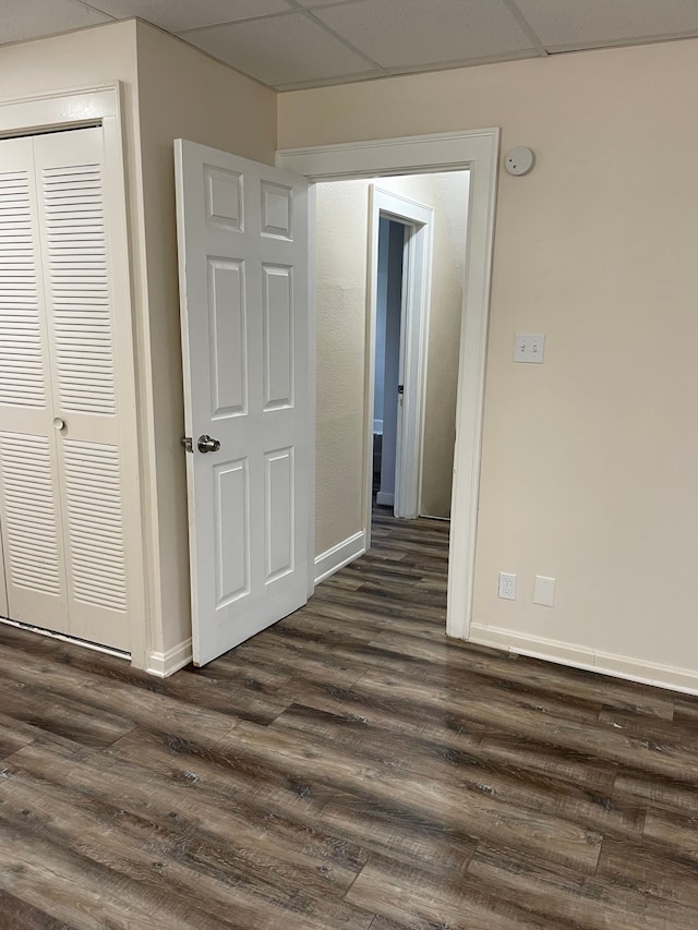 unfurnished room with dark wood-style flooring, a drop ceiling, and baseboards