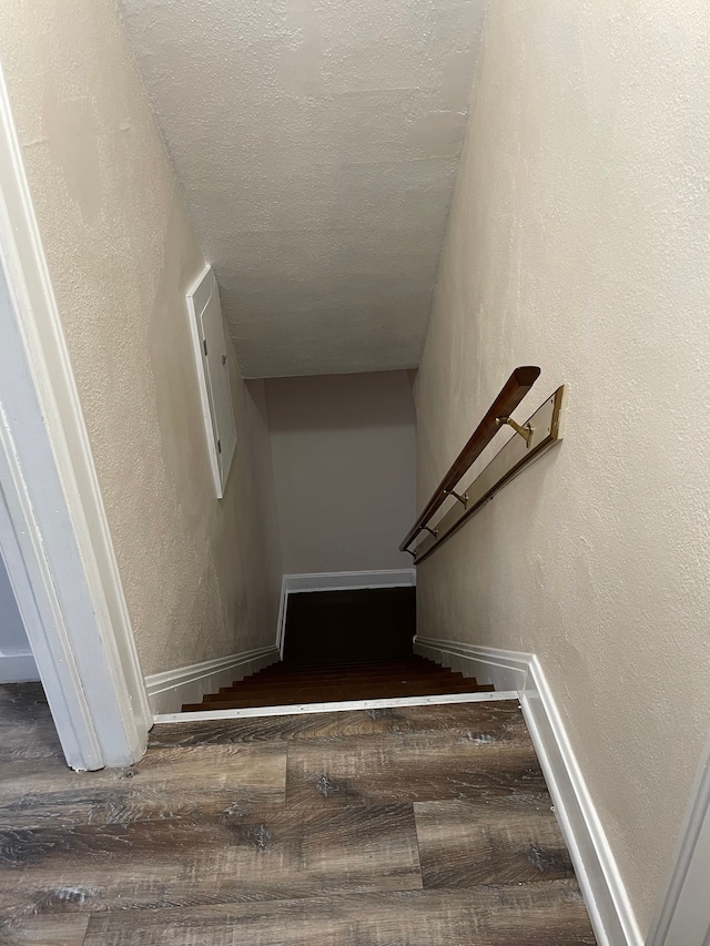 stairs with a textured ceiling, a textured wall, wood finished floors, and baseboards