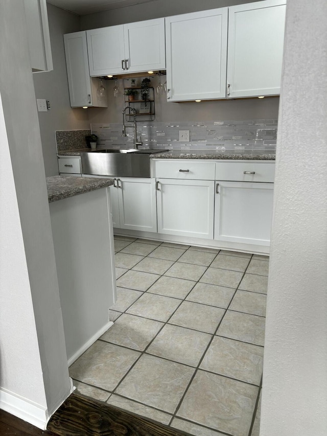 kitchen featuring light tile patterned floors, dark stone counters, a sink, and white cabinets