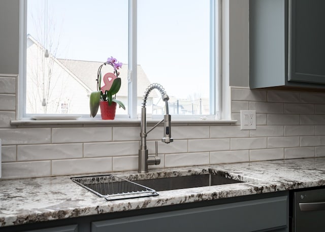 kitchen with light stone counters, gray cabinets, a sink, and tasteful backsplash