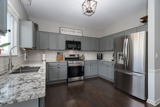 kitchen with dark wood finished floors, stainless steel appliances, gray cabinets, a sink, and light stone countertops