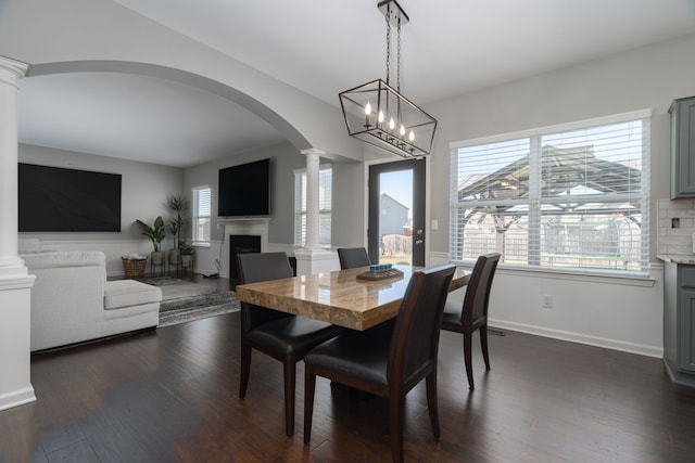 dining space featuring ornate columns, a fireplace, a wealth of natural light, and dark wood-type flooring