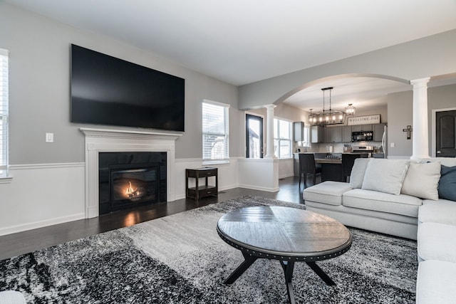 living room with decorative columns, baseboards, dark wood-type flooring, and a tiled fireplace