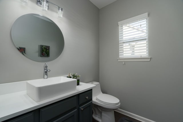 half bathroom featuring vanity, toilet, and baseboards