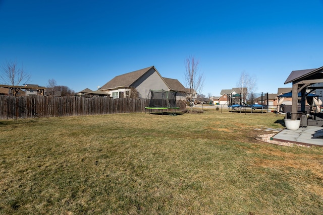 view of yard with a trampoline, fence, and a patio