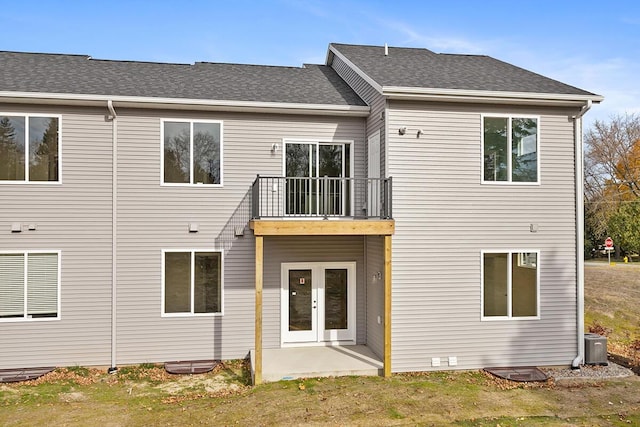 back of property featuring cooling unit, a balcony, french doors, roof with shingles, and a lawn