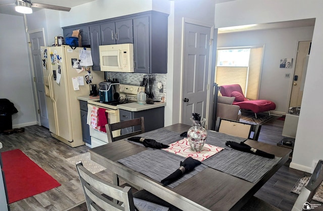 kitchen featuring light countertops, backsplash, wood finished floors, white appliances, and baseboards