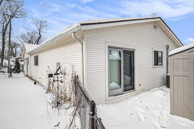 snow covered property with a shed, fence, and an outdoor structure