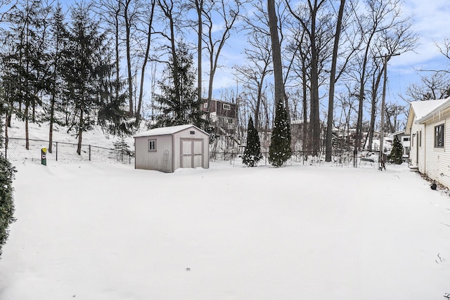 yard covered in snow featuring a garage, an outbuilding, a fenced backyard, and a storage shed