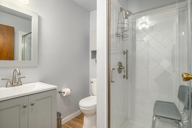 bathroom featuring toilet, wood finished floors, vanity, baseboards, and a stall shower