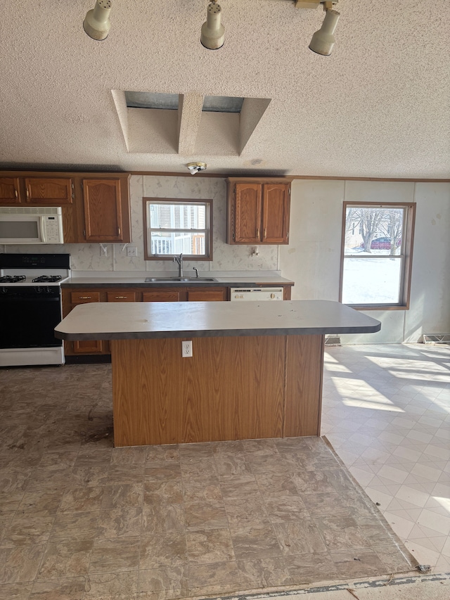 kitchen with a wealth of natural light, a center island, white appliances, and a sink