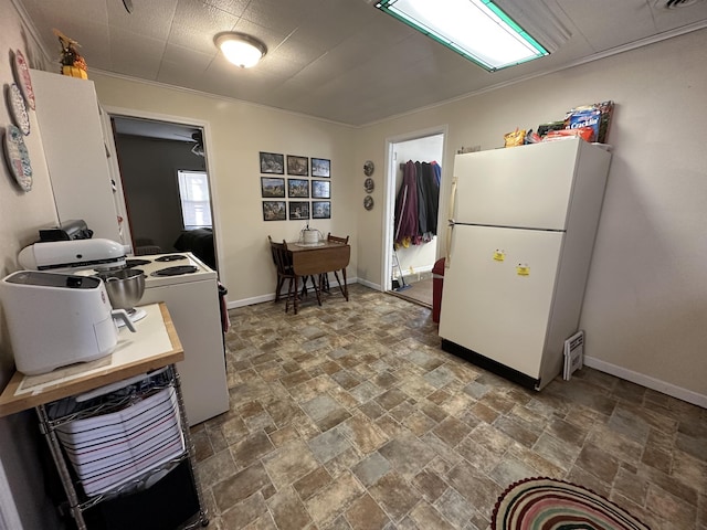 kitchen with stone finish flooring, range with electric stovetop, freestanding refrigerator, and baseboards