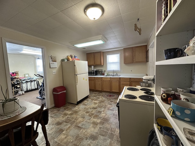 kitchen with white appliances, brown cabinetry, a sink, light countertops, and stone finish floor