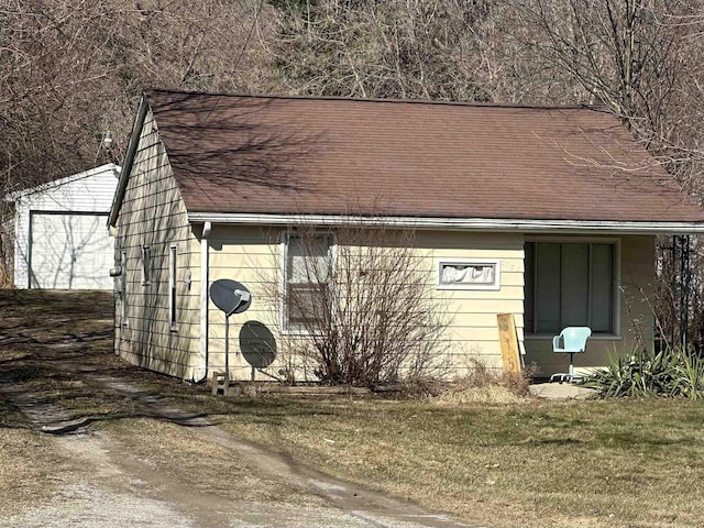 view of side of property with an outdoor structure, a lawn, and a shingled roof