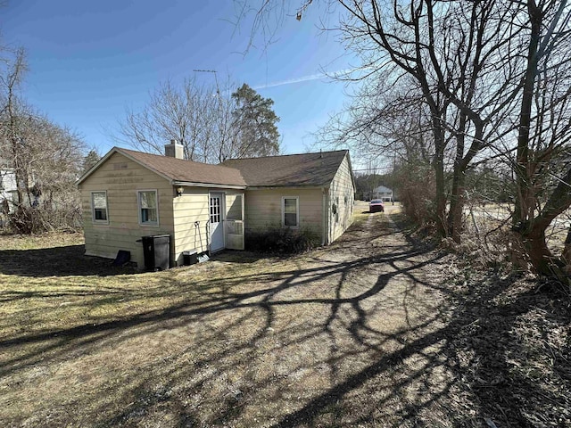 view of property exterior featuring a chimney, a yard, and a shingled roof