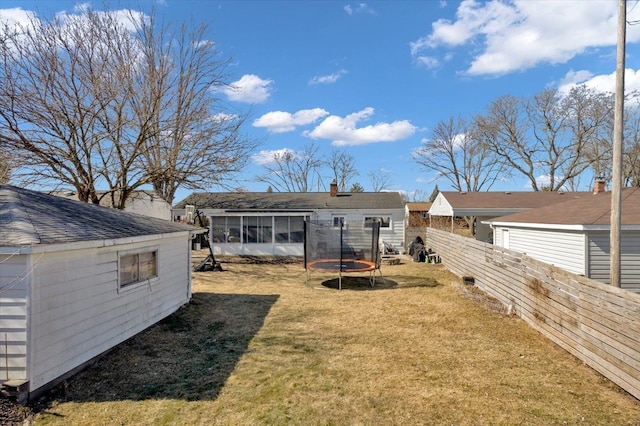 rear view of property featuring a trampoline, a lawn, fence, and a sunroom