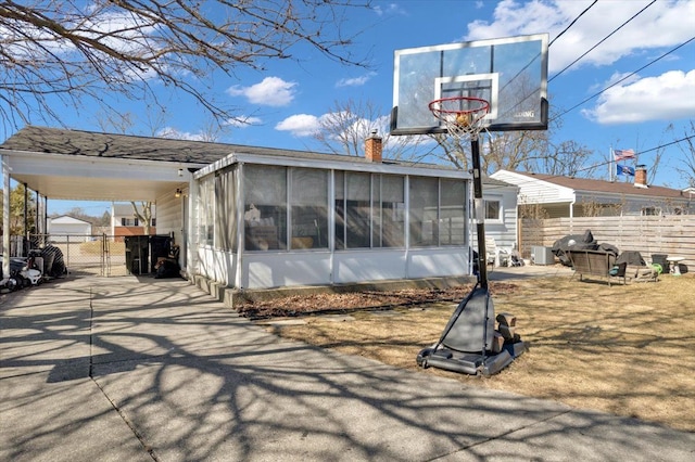 rear view of house featuring an attached carport, driveway, a sunroom, and fence