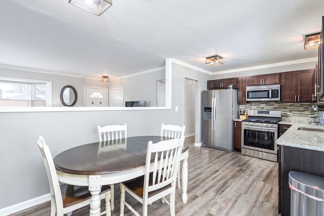 kitchen with light wood finished floors, ornamental molding, stainless steel appliances, dark brown cabinetry, and tasteful backsplash