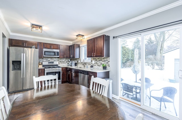 kitchen with a sink, dark brown cabinets, appliances with stainless steel finishes, crown molding, and tasteful backsplash