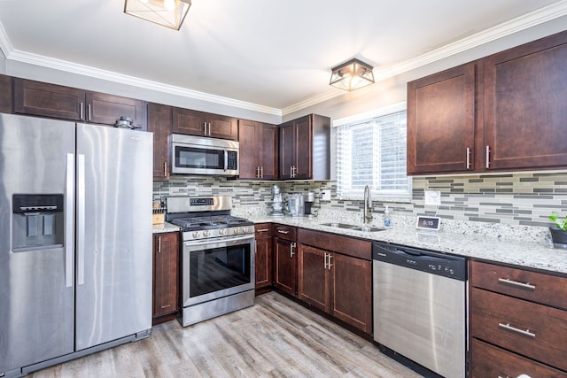 kitchen with light wood-style flooring, ornamental molding, a sink, appliances with stainless steel finishes, and decorative backsplash