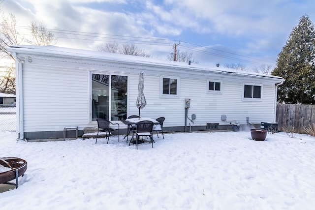 snow covered rear of property featuring a fire pit and fence