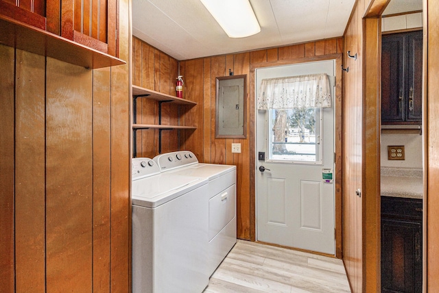 washroom with washer and clothes dryer, light wood-style floors, wood walls, laundry area, and electric panel