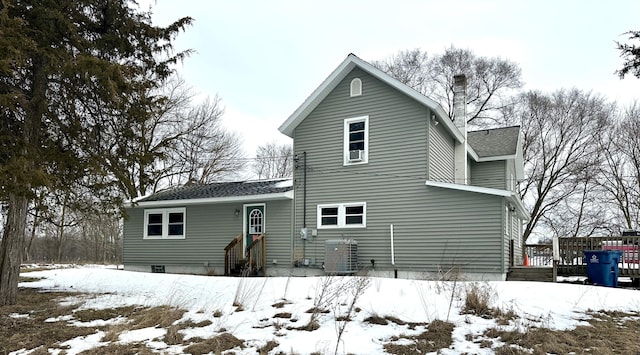 snow covered rear of property featuring a shingled roof and central air condition unit