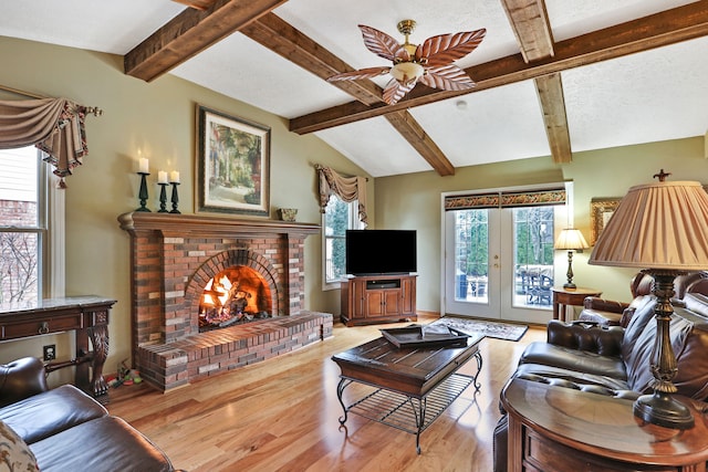 living room featuring a ceiling fan, wood finished floors, vaulted ceiling with beams, a textured ceiling, and a brick fireplace