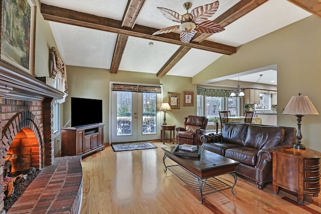 living room with lofted ceiling with beams, light wood-style flooring, a textured ceiling, french doors, and a fireplace