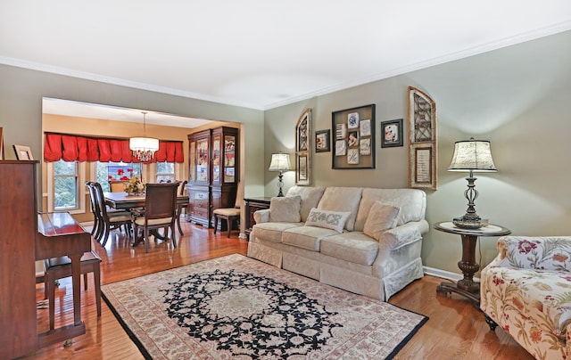 living room with an inviting chandelier, crown molding, baseboards, and wood finished floors