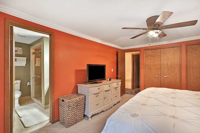 bedroom with a ceiling fan, light colored carpet, ensuite bath, crown molding, and two closets