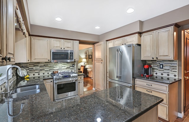 kitchen featuring decorative backsplash, appliances with stainless steel finishes, a sink, dark stone counters, and a peninsula