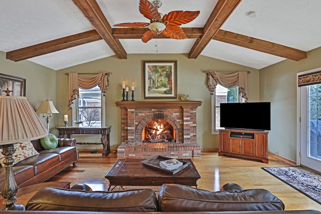 living area featuring vaulted ceiling with beams, a brick fireplace, and a healthy amount of sunlight