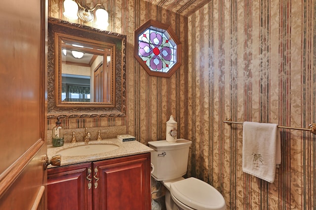 half bathroom featuring toilet, wallpapered walls, and vanity