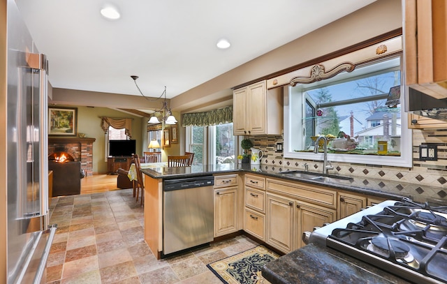 kitchen featuring tasteful backsplash, a sink, stainless steel appliances, a fireplace, and a notable chandelier