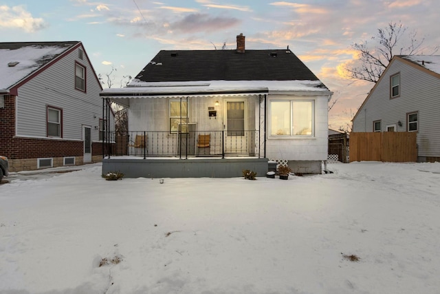 snow covered house featuring a porch, fence, and a chimney