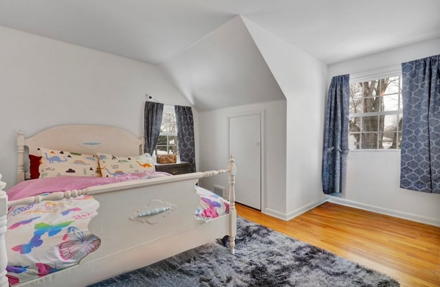 bedroom with vaulted ceiling, multiple windows, wood finished floors, and baseboards