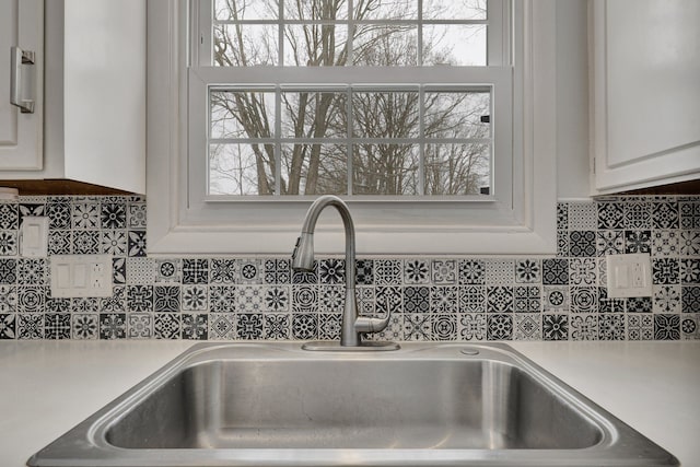 details featuring tasteful backsplash, white cabinetry, light countertops, and a sink