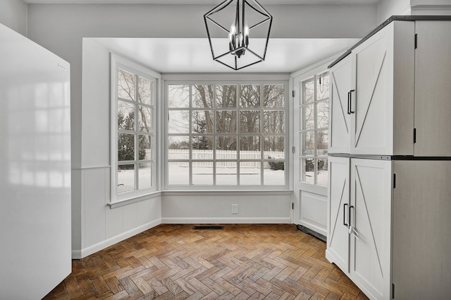 unfurnished dining area with baseboards, plenty of natural light, visible vents, and a notable chandelier